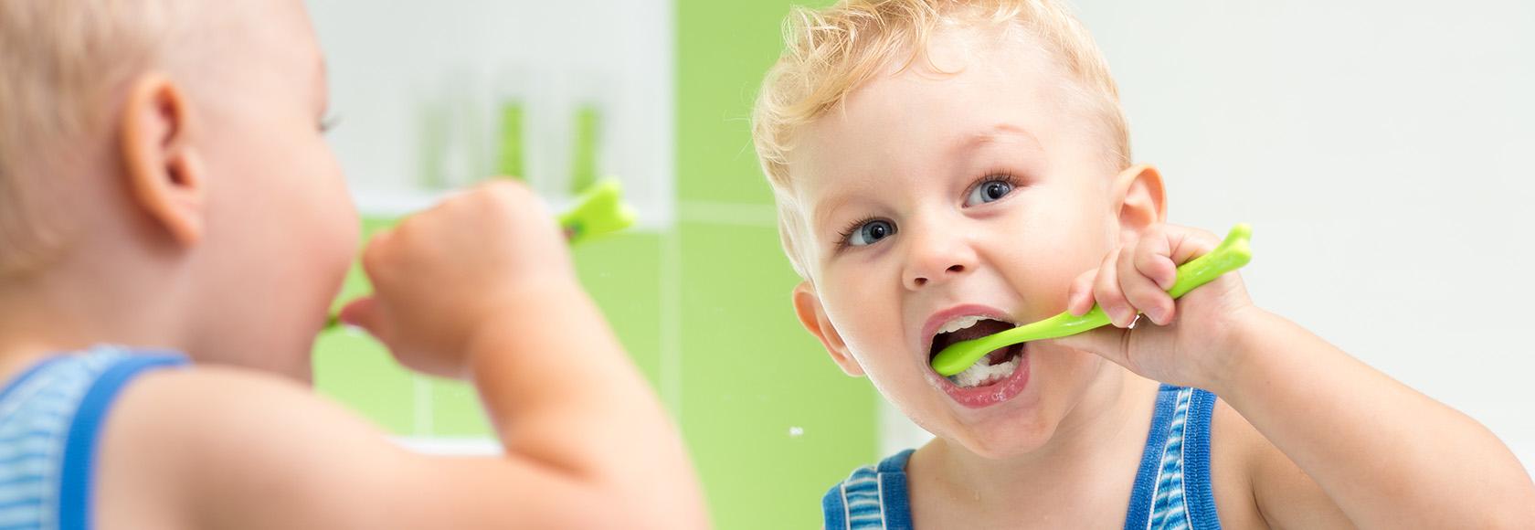 Mały chłopiec myjący zęby w łazience. Odbicie w lustrze.