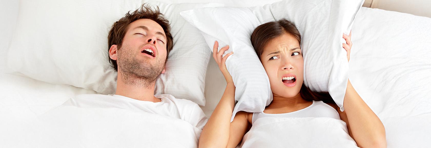 mężczyzna chrapie, obok kobieta poduszką zakrywa uszy