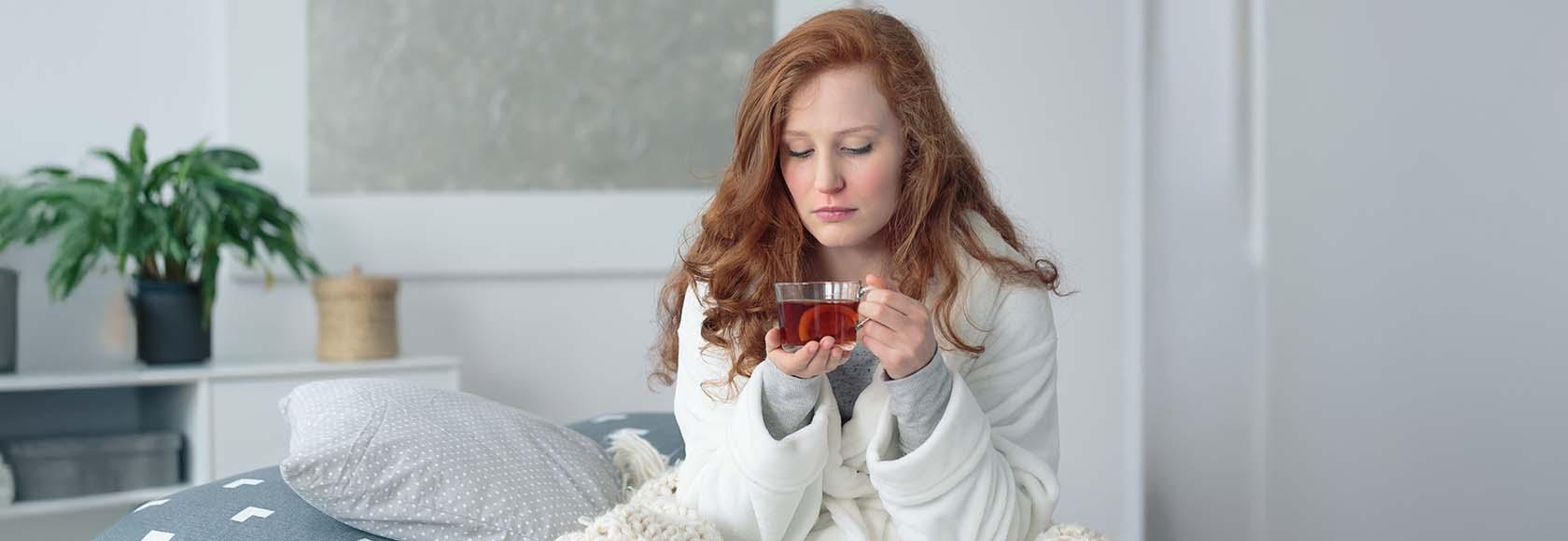 Młoda kobieta siedzi na łóżku z kubkiem herbaty