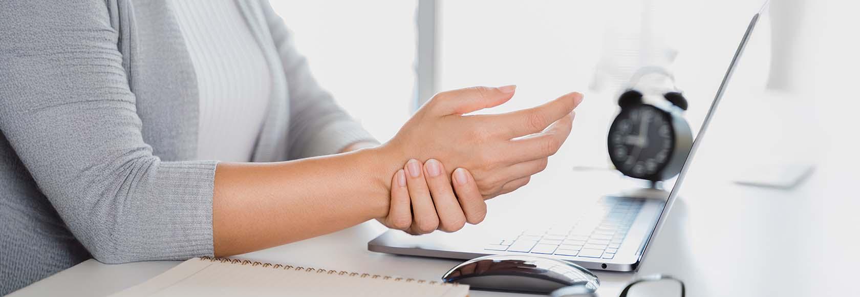 kobieta przy komputerze trzyma się za rękę