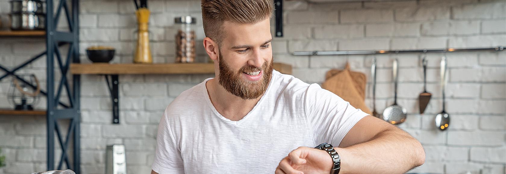 Młody mężczyzna w kuchni patrzy na zegarek 