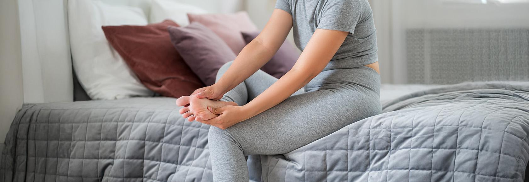 kobieta siedzi na tapczanie i masuje sobie stopę