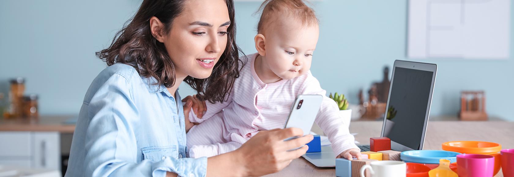 Mama z dzieckiem przy stole. Mama przegląda telefon, a dziecko bawi się klockami.