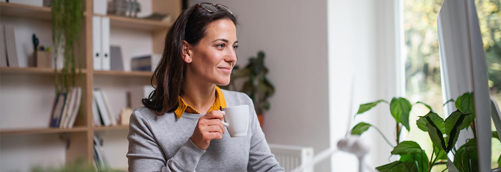 Kobieta z kubkiem kawy w domu przed komputerem