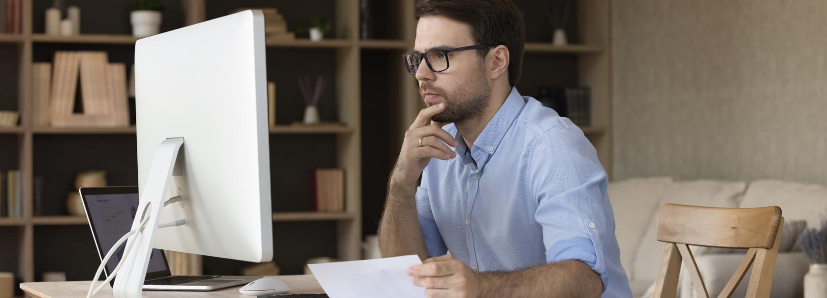 Mężczyzna z papierami przed komputerem