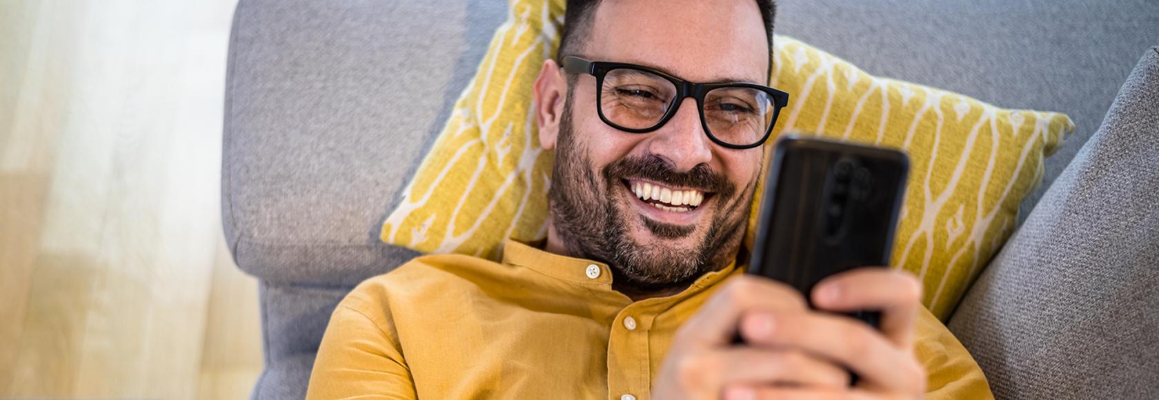 Mężczyzna w żółtej koszuli leży na kanapie z telefonem