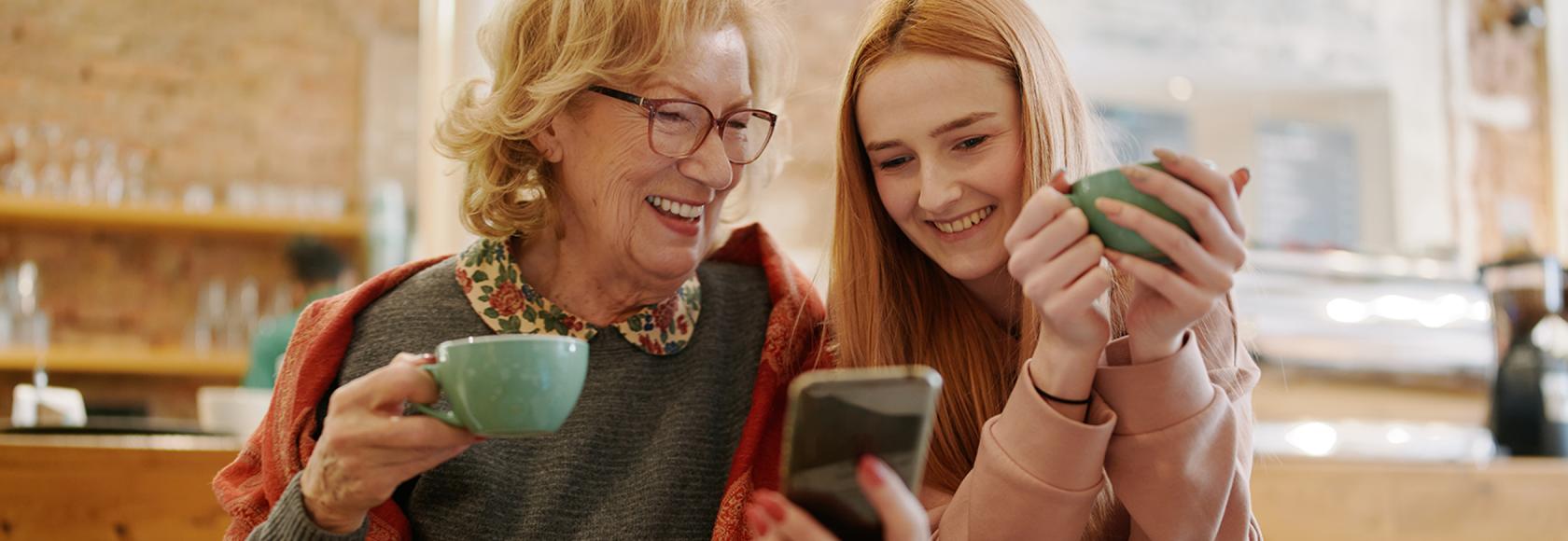 Babcia i wnuczka patrzą na telefon komórkowy, pijąc herbatę w kuchni