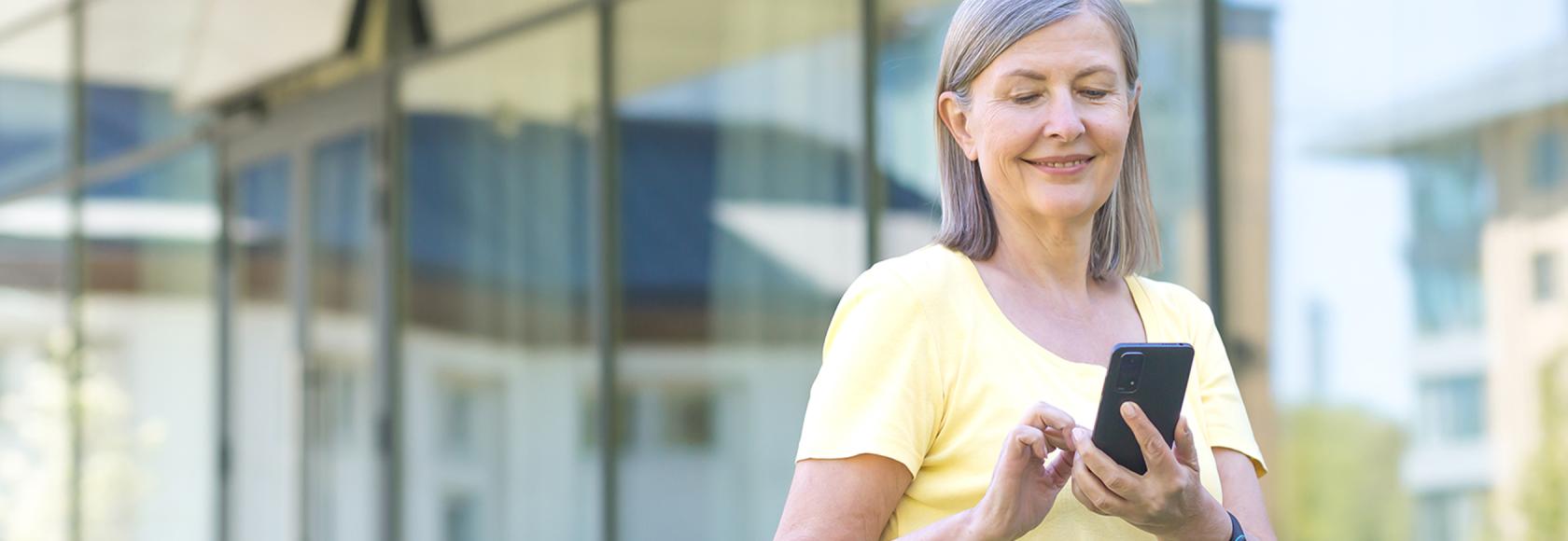 Kobieta przed biurowcem sprawdza coś w komorce