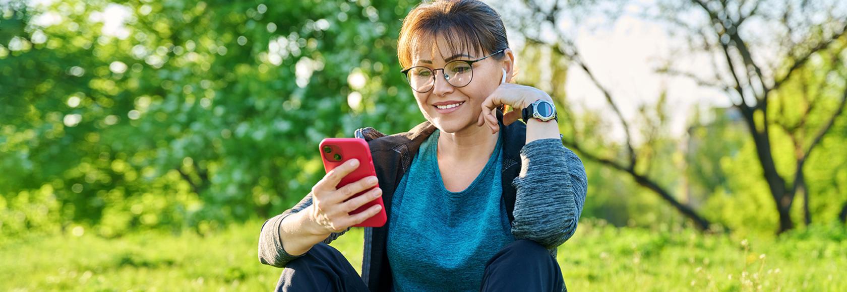Pani siedząca na trawie z uśmiechem patrzy na telefon
