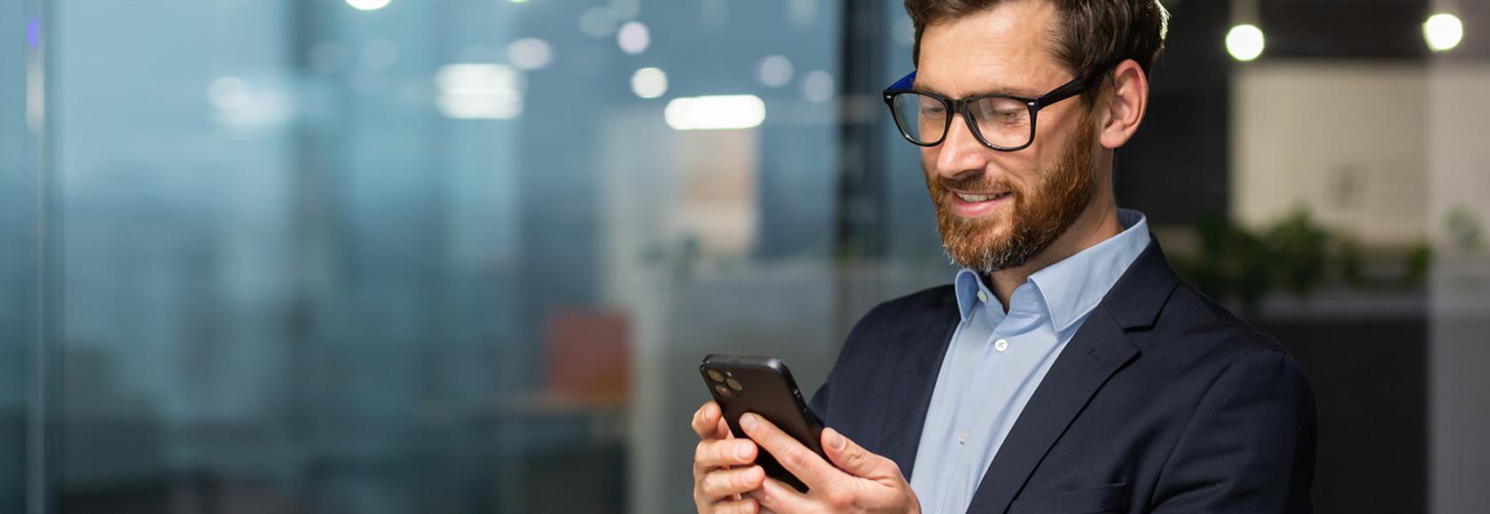 młody brodaty facet z komórką przed bankiem