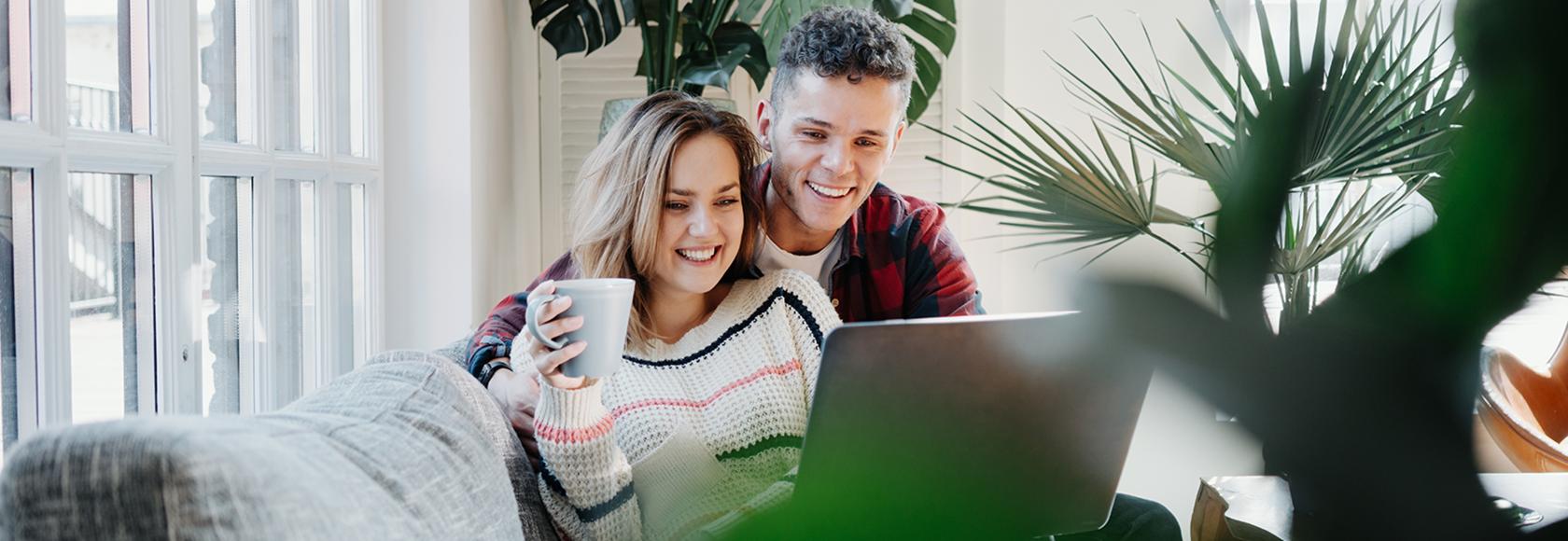 uśmiechnięta para młodych na kanapie przed laptopem