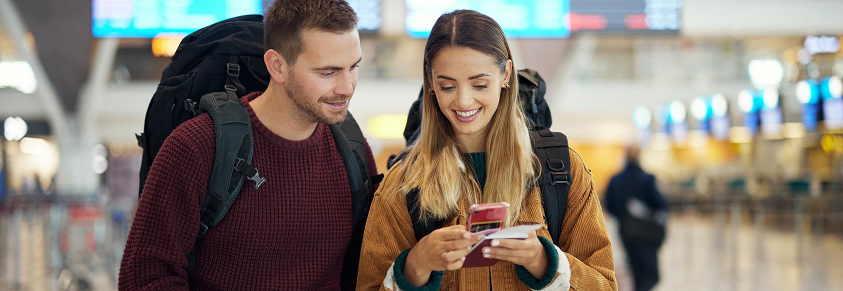 mlodzi ludzie na lotnisku z plecakami patrza na telefon