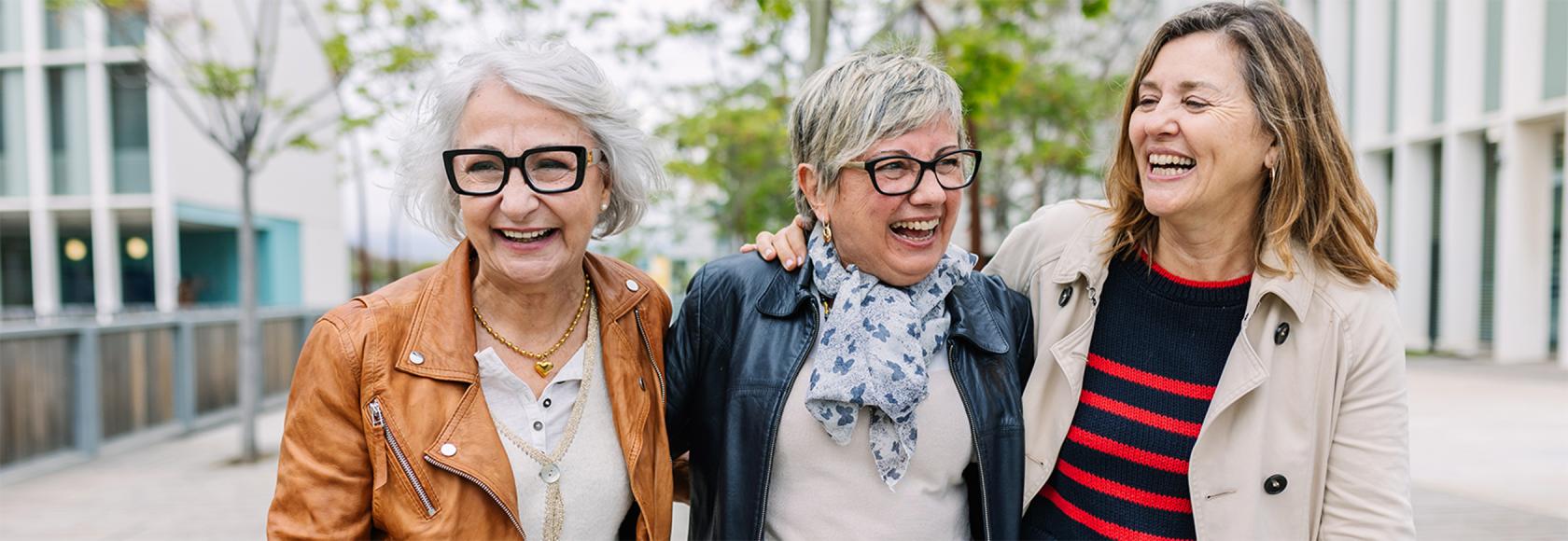 trzy panie w roznym wieku ida ulica rozesmiane i objete 