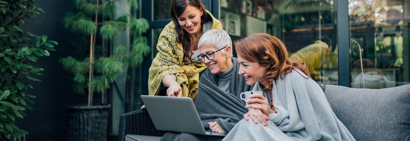 trzy przyjaciółki, jedna pokazuje coś dwóm pozostałym na laptopie