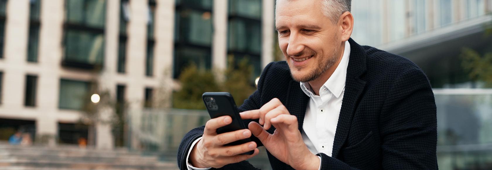 Mężczyzna w garniturze z telefonem siedzi przed biurowcem