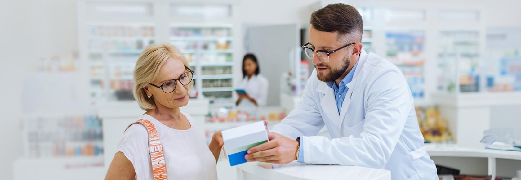 farmaceuta tłumaczy coś starszej pacjentce z lekiem w ręku