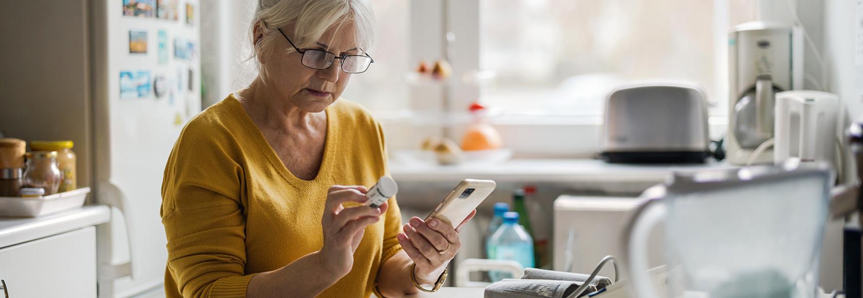 starsza pani w kuchni z pojemnikiem leków i komórką w rękach
