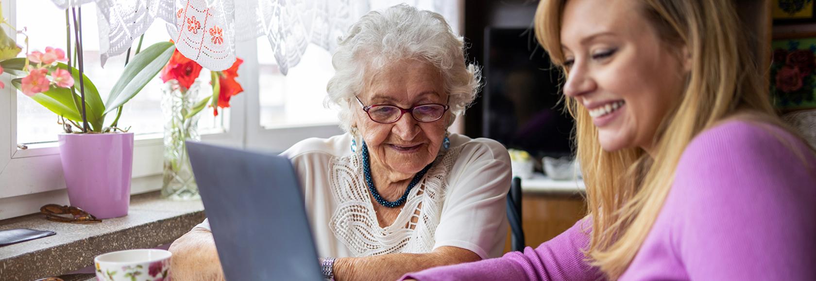 Babcia i wnuczka siedzą przy stole z herbatą i komputerem