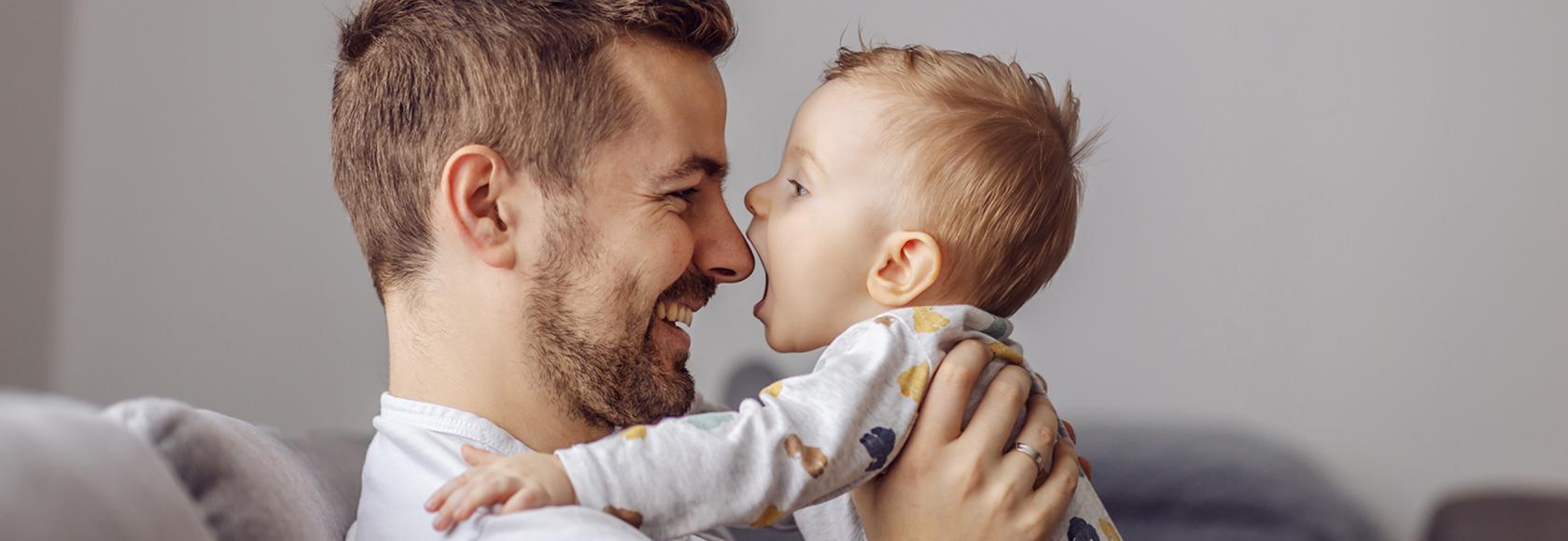Tata z małym dzieckiem, trzyma je w ramionach i patrzą na siebie