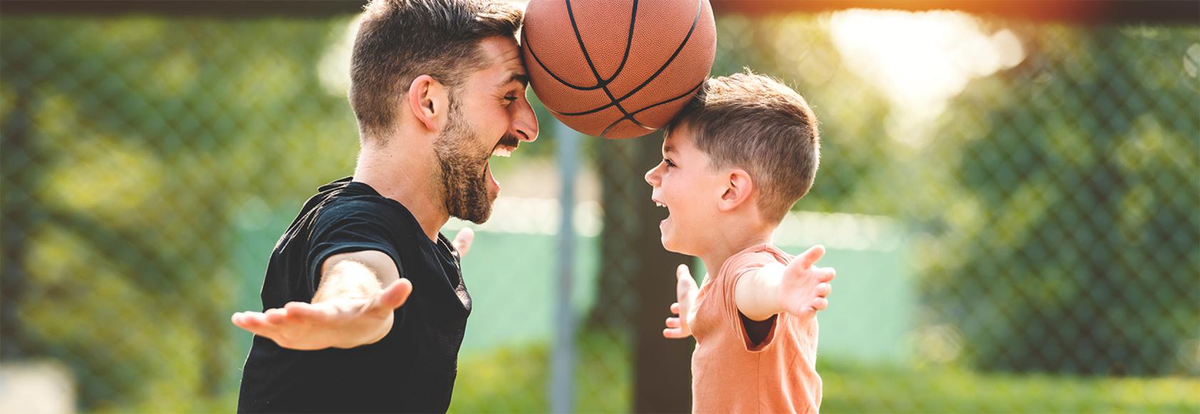 Ojciec z synem trzymają czołami piłkę do kosza