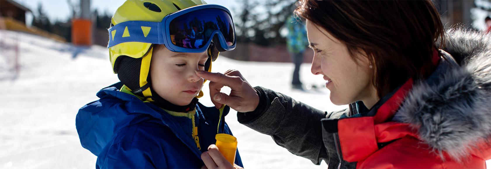 mama smaruje dziecku nos, oboje na stoku narciarskim