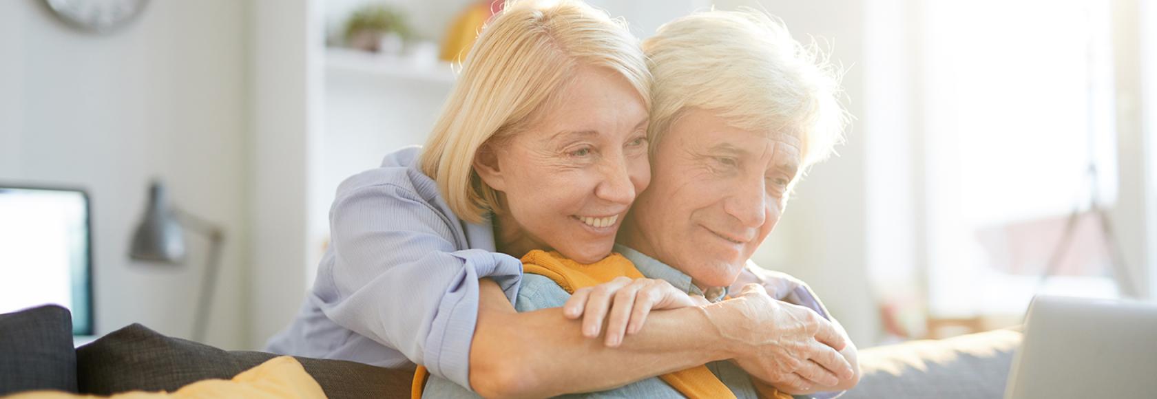 50letnia pani obejmuje za szyję męza, on patrz w laptop