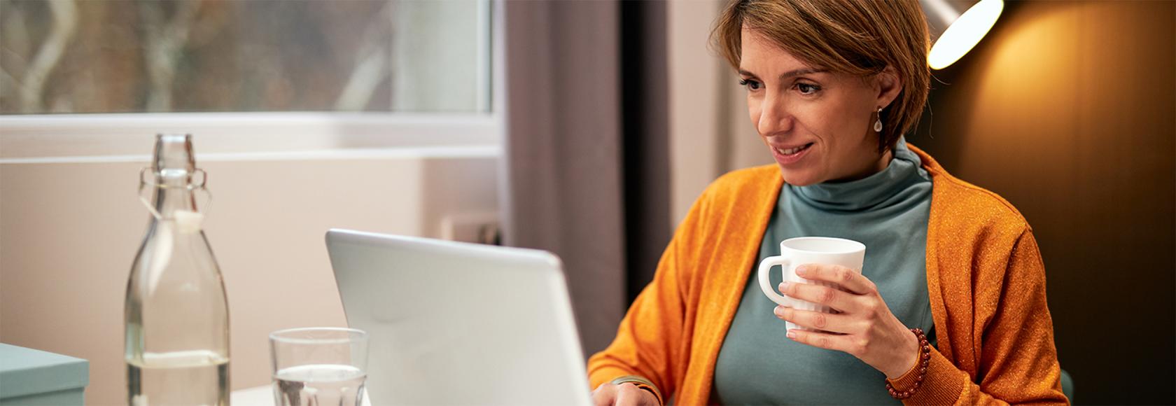 kobieta w sweterku na golfie przy stole z laptopem i herbatą