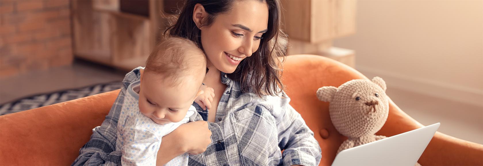 Matka z rocznym dzieckiem na kanapie, laptop ma na kolanach