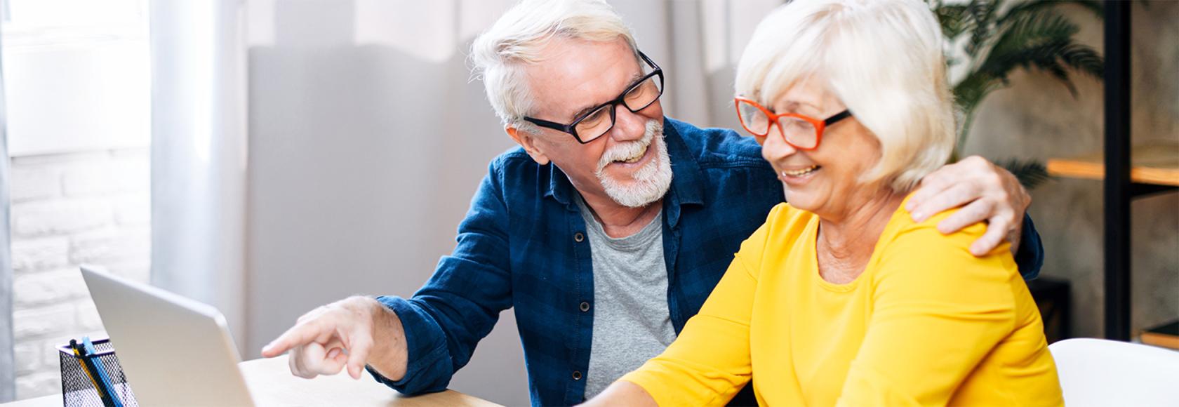 para starszych osób, Pan pokazuje z uśmiechem na treść na laptopie pani