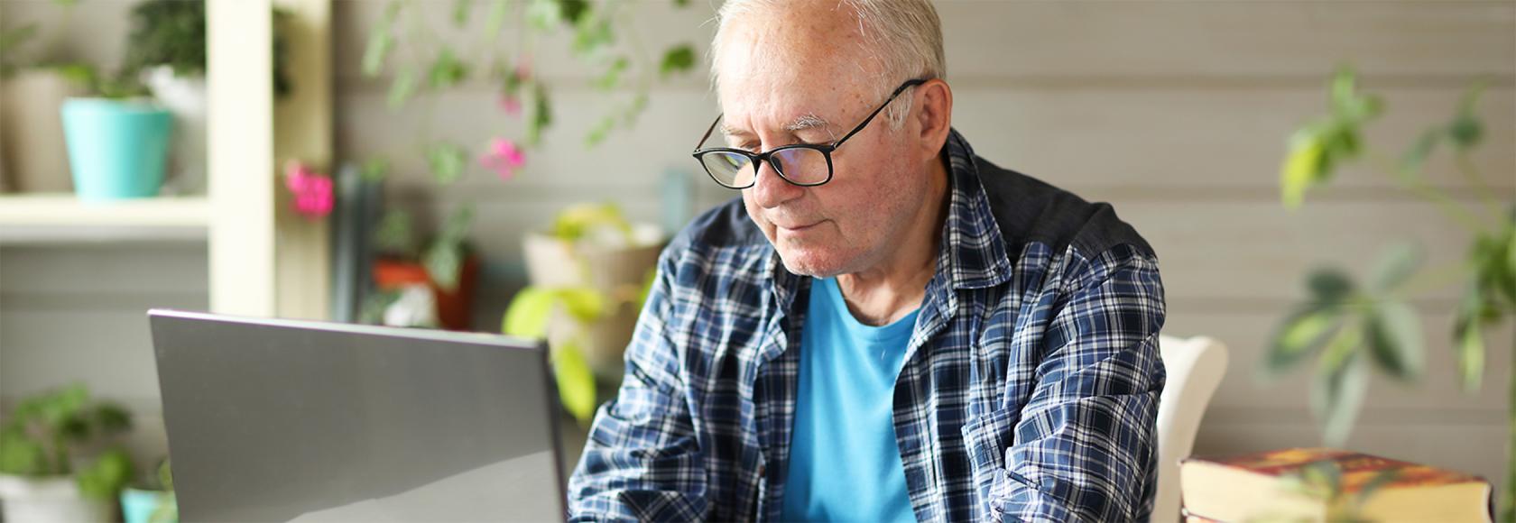 Starszy, siwy pan we flanelowej koszuli przed komputerem