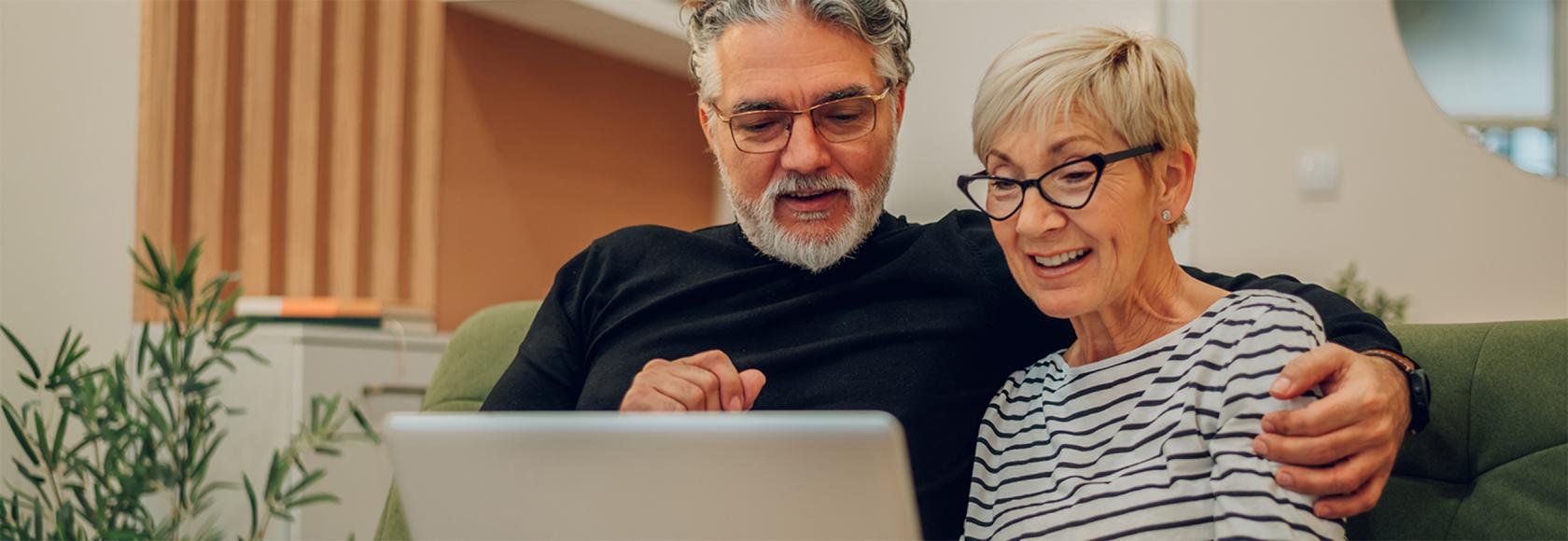 Para 50latków z laptopem na kanapie, on ją obejmuje ramieniem 