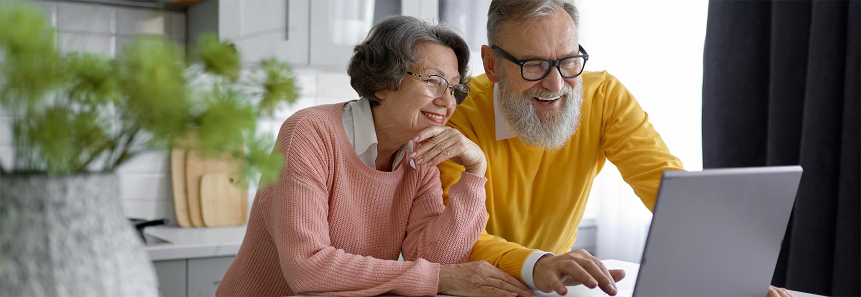 Para w średnum wieku z uśmiechem zagląda do laptopa