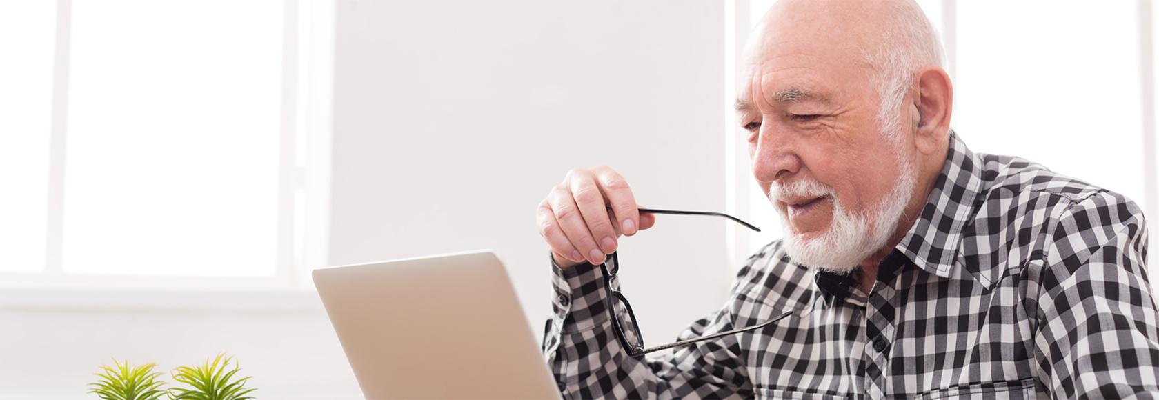 Starszy pan z brodą i okularami w ręku przed komputerem