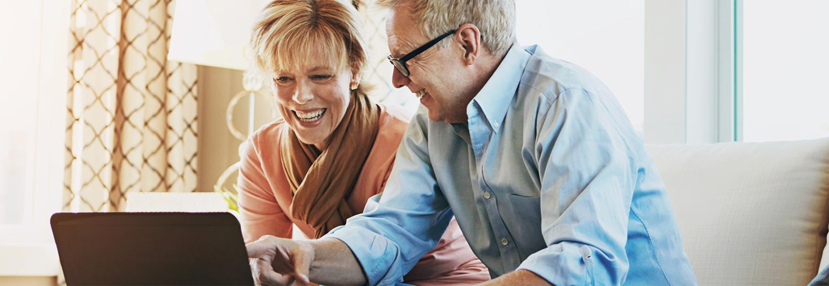 Mąż pokazuje żonie coś na laptopie, oboje na kanapie