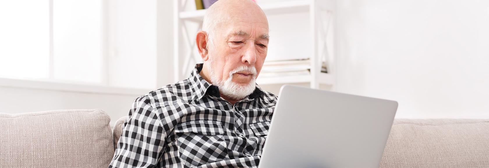 Starszy pan z broda z laptopem na kolanach na kanapie