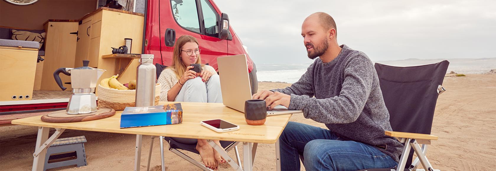 para przed kamperem, mężczyzna przy laptopie, w tle plaża