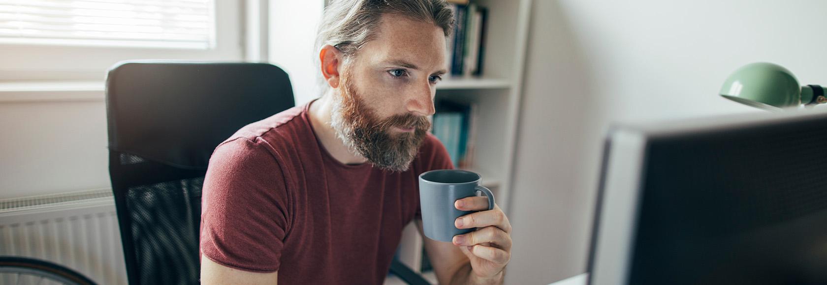 Brodaty mężczyzna z kubkiem przed laptopem