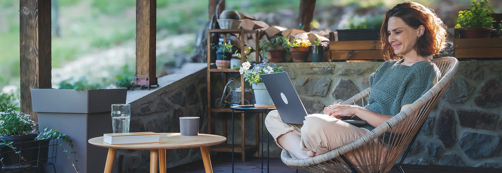 Kobieta na werandzie w wiklinowym fotelu z laptopem