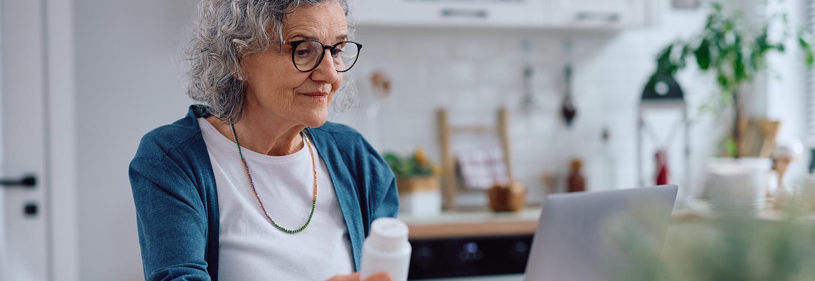 starsza pani przy komputerze z opakowaniem leku w  ręku 