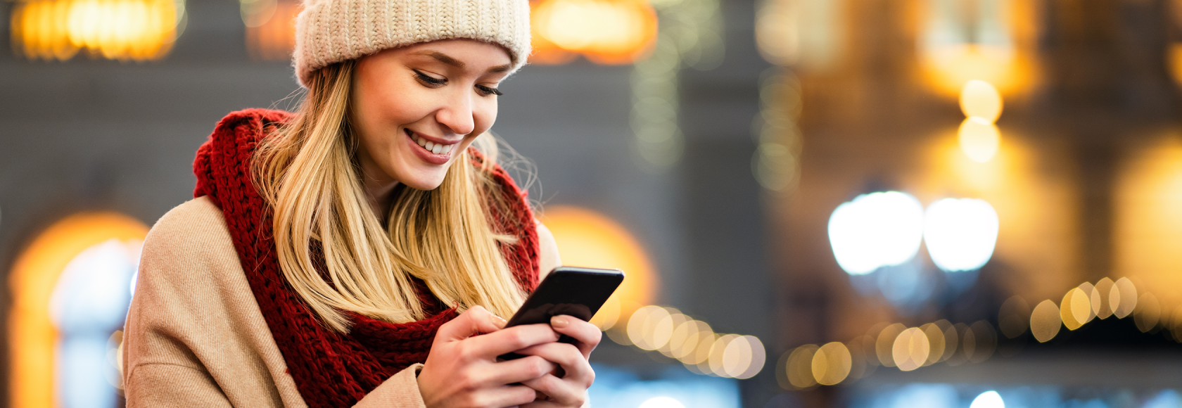 Kobieta z komórką, w czapce, w tle nocne miasto