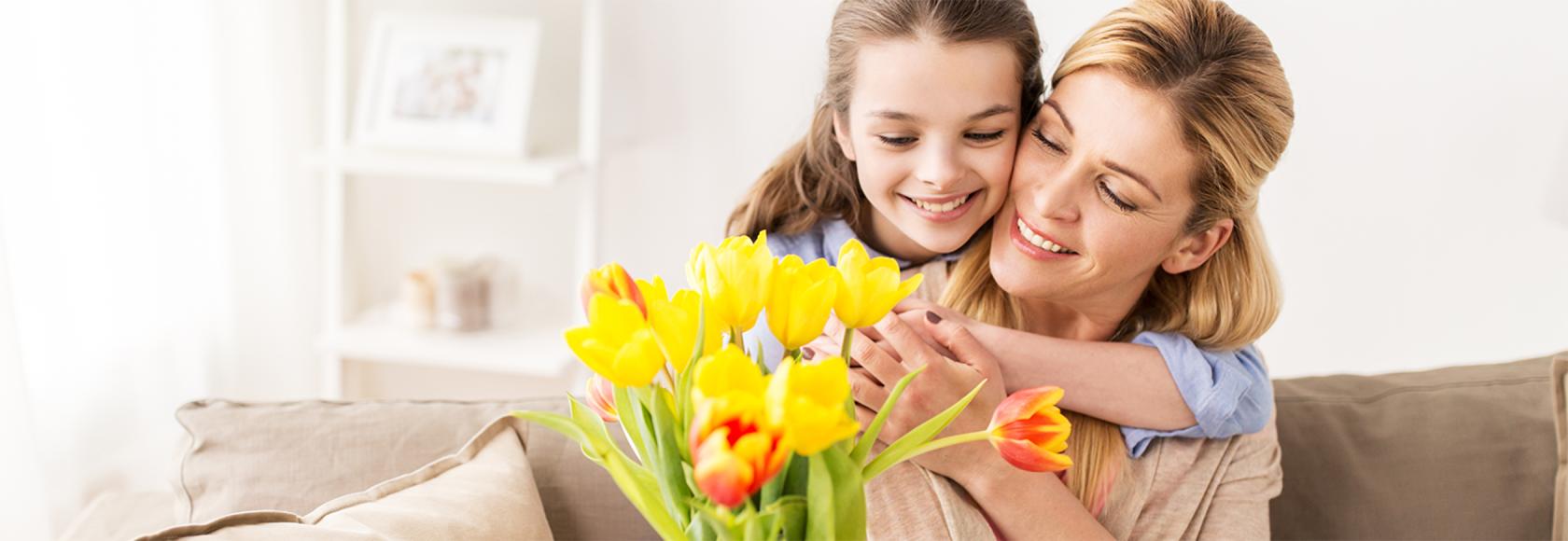 dziewczynka obejmuje mamę i wręcza jej kwiaty
