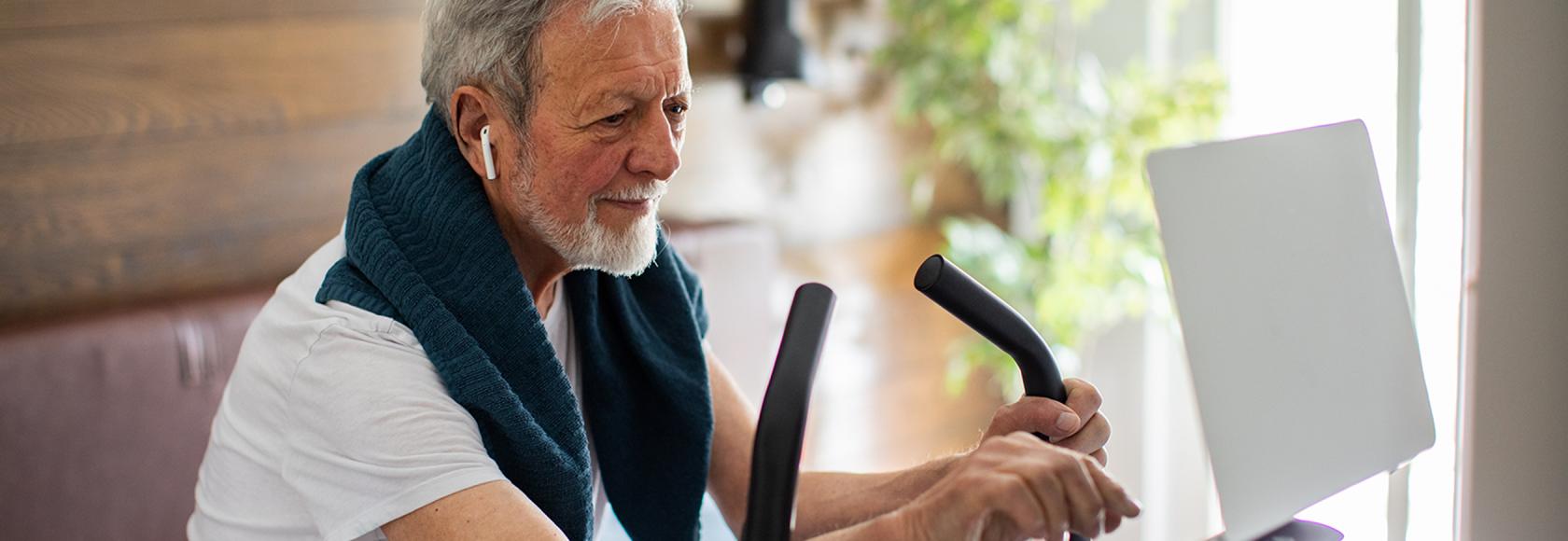 Starszy pan na orbitreku i z laptopem