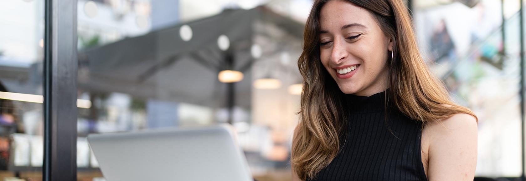 uśmiechnięta kobieta przed laptopem, ma długie włosy