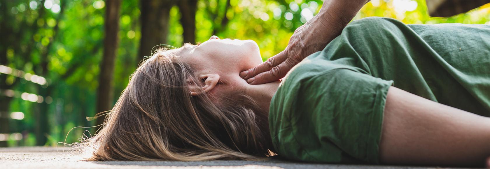 ktoś sprawdza, czy leżąca na szosie dziewczyna ma puls, lato, krótkie rękawki, zieleń w tle