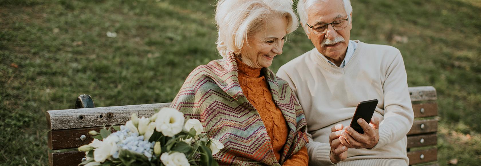 Starsza para na ławce, on pokazuje jej coś w telefonie