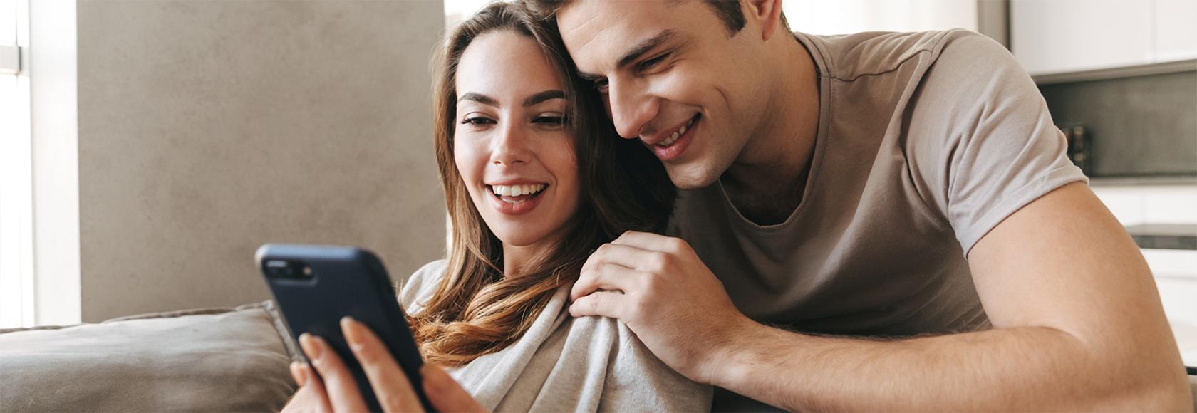 ona siedzi na kanapie i pokazuje mu coś na komorce, on pochyla się nad nią i zagląda jej przez ramię