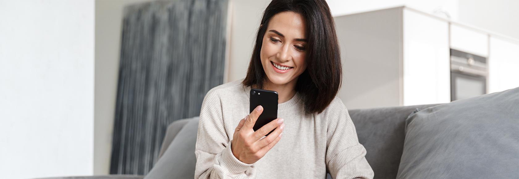 Kobieta na kanapie siedzi po turecku, ma komórkę