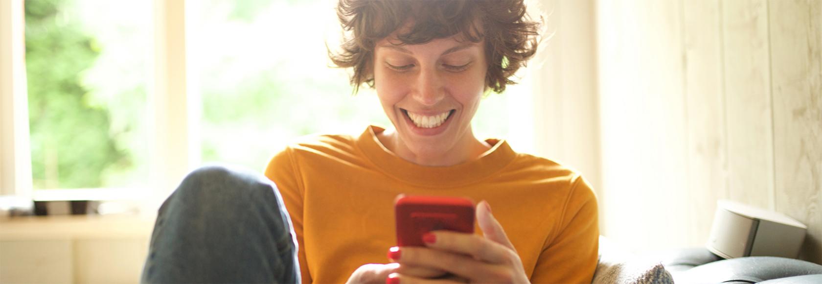 Roześmiana dziewczyna trzyma w ręku telefon i patrzy na ekran