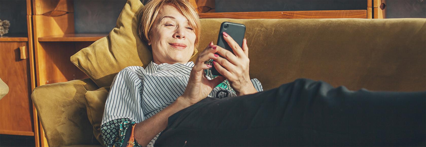 Ruda 50latka na kanapie z telefonem