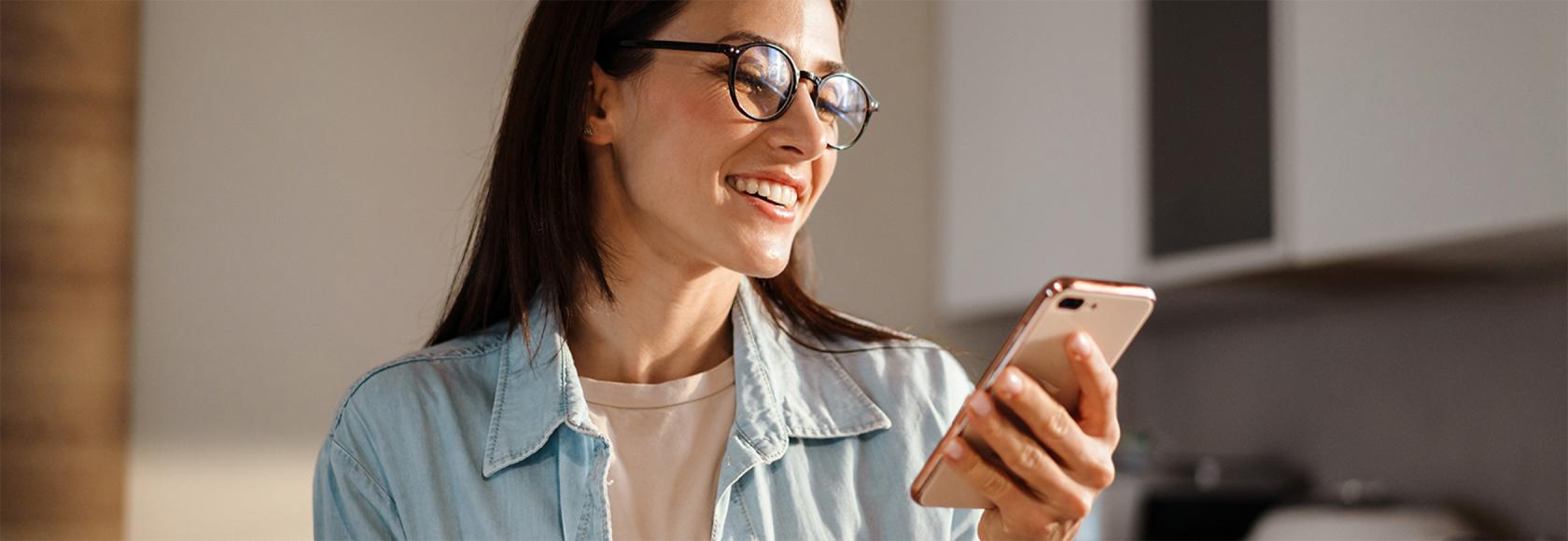 W kuchni kobieta z uśmiechem patrzy na komórkę